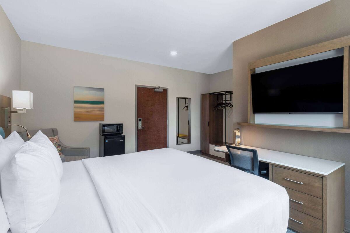 Une chambre d’hôtel avec un grand lit, un bureau avec une chaise, une télévision, un miroir et une porte.