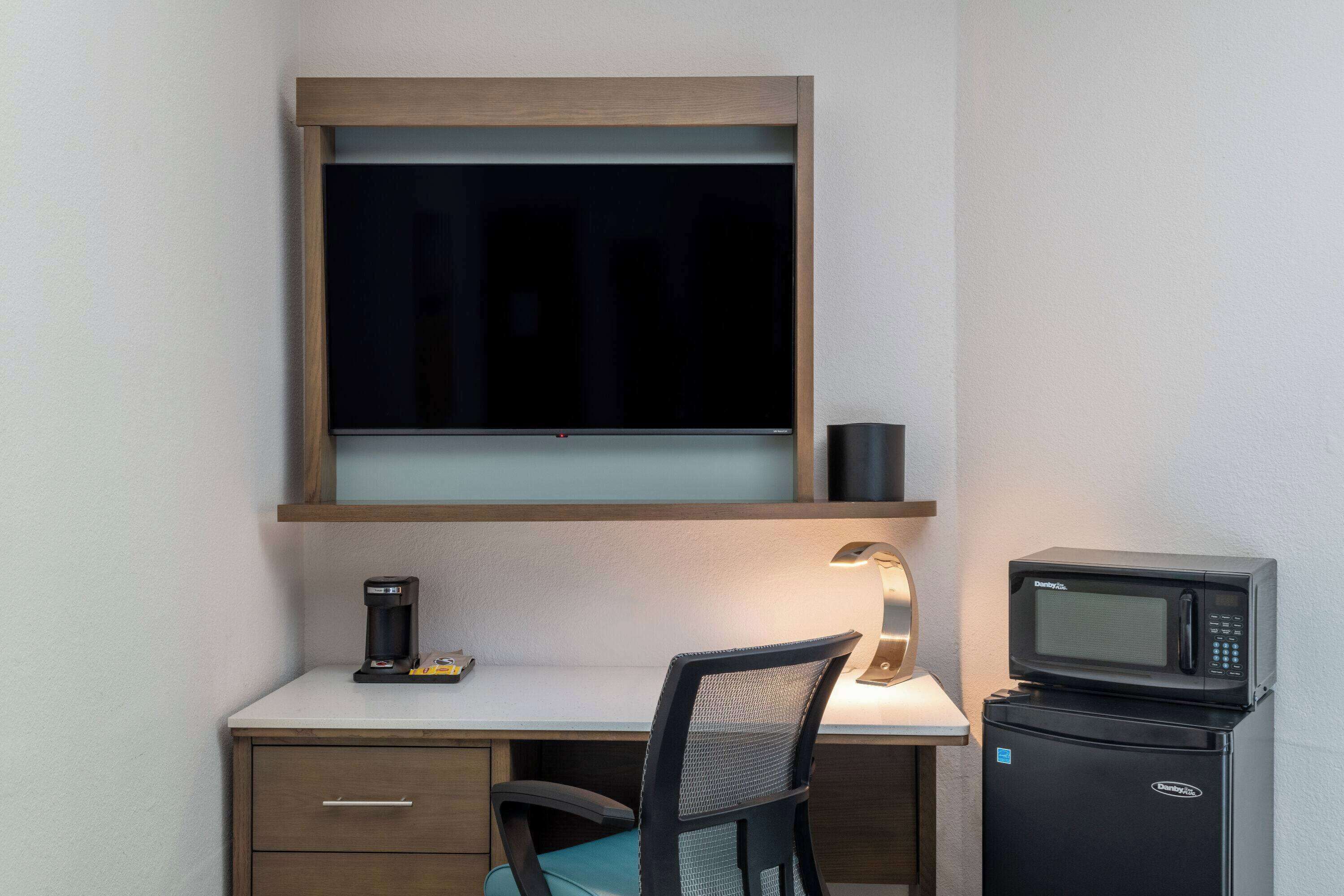 A compact workspace with a desk, chair, coffee maker, and microwave.
