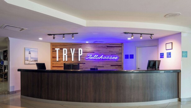 A reception desk with a wooden panel and a neon sign reading "TRYP Tallahassee".