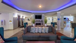 A modern lobby with a grey sofa, teal armchairs, a flat-screen TV, and a fireplace.