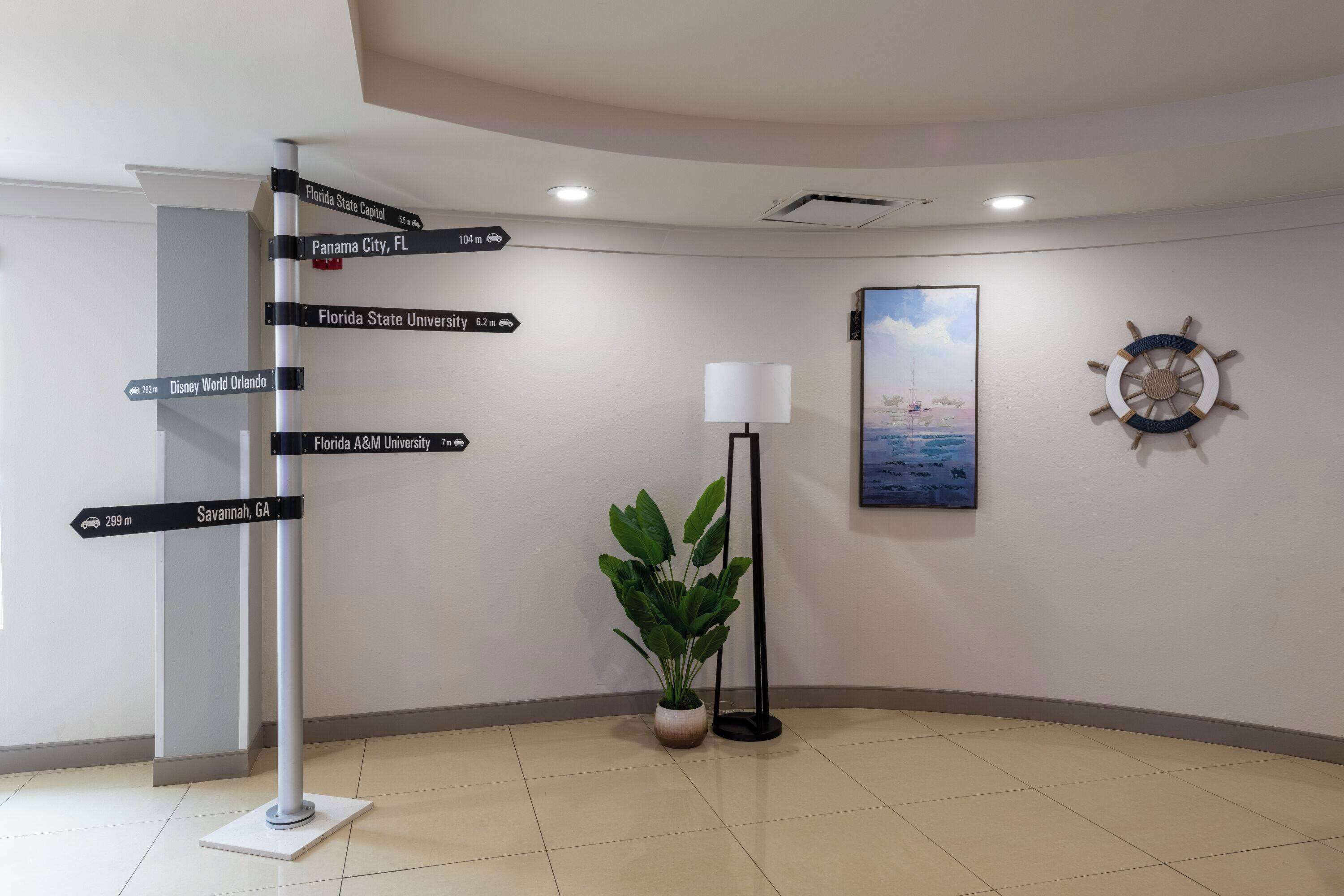 A lobby with a directional signpost, a potted plant, a floor lamp, a painting, and a ship's wheel decoration.