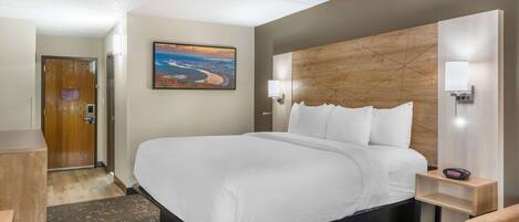 A hotel room with a large bed, a desk, a chair, a nightstand, and a painting on the wall.