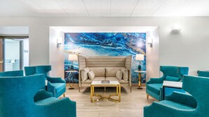 Zona relax moderna con poltrone rivestite in verde acqua, un divano beige e un tavolino da caffè con cornice dorata.