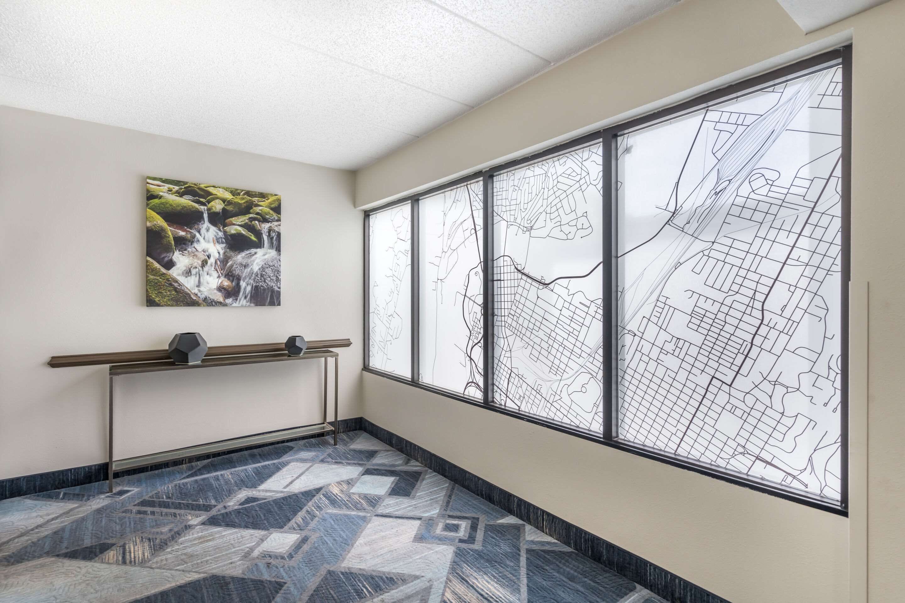 A hallway with a patterned floor, a map on the wall, and a painting of a waterfall.
