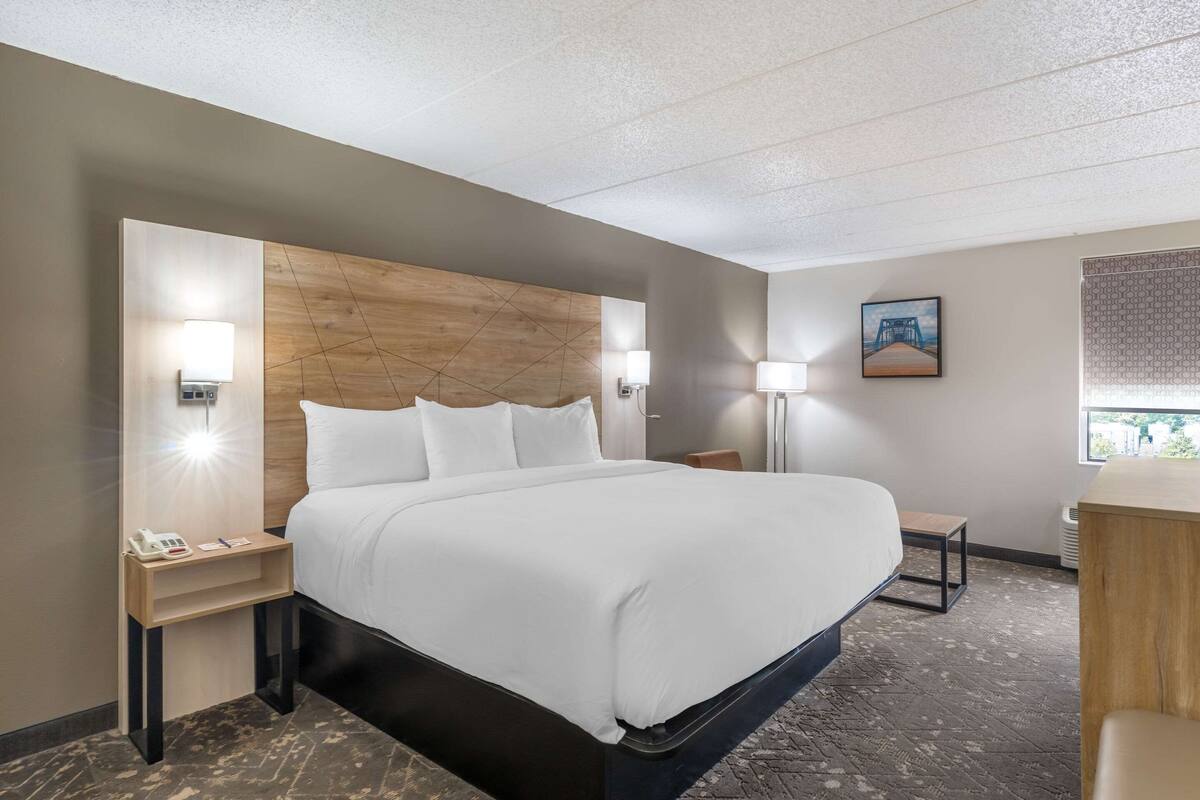 A hotel room with a large bed, bedside tables, a desk, and a window.