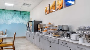 Una cucina moderna con un lungo bancone, dotata di diversi elettrodomestici e una macchina da caffè. Nell'area pranzo adiacente si trovano sedie e un tavolo.