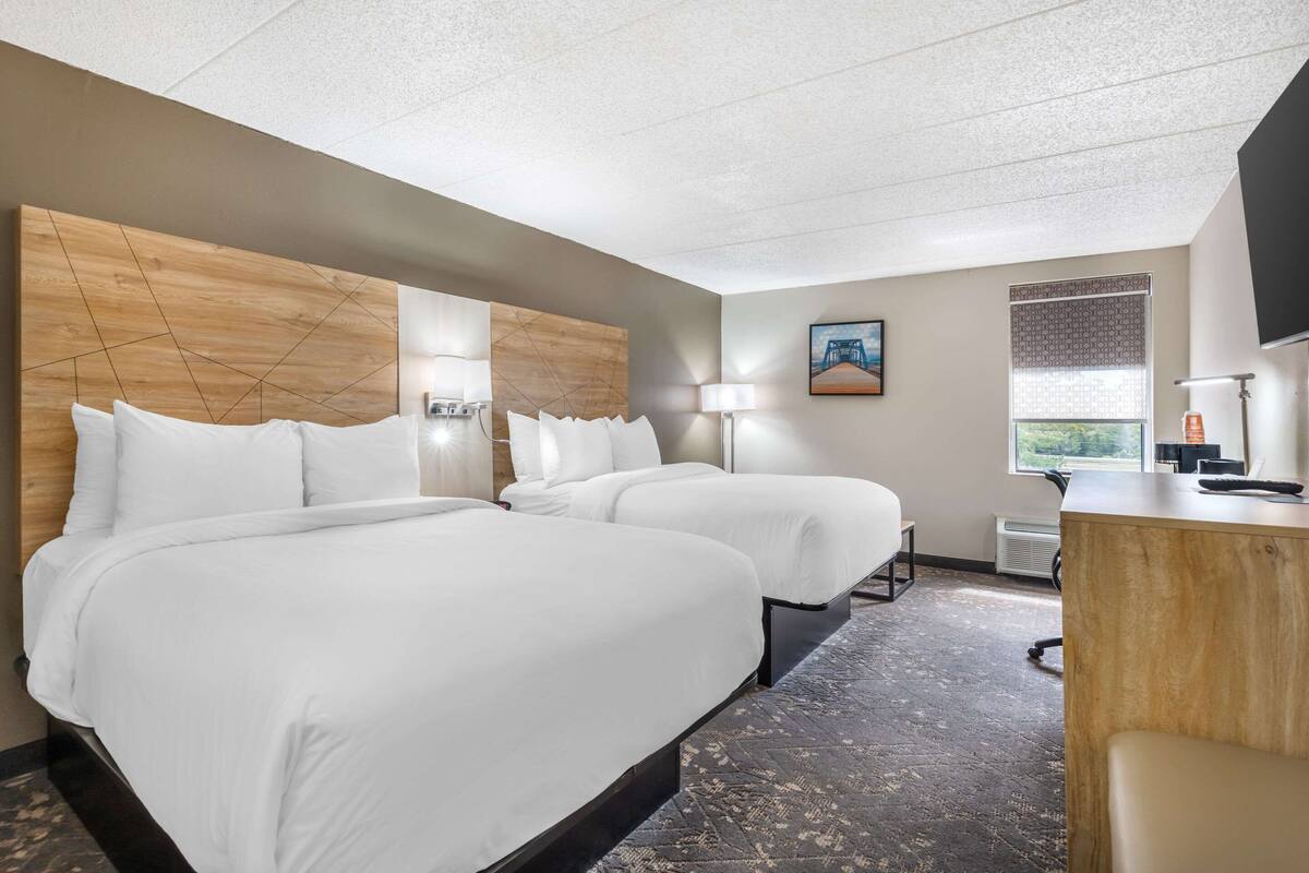 A hotel room with two beds, a desk, a chair, a TV, and a window with a view.