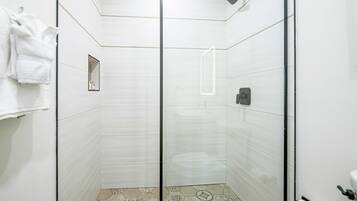 Una cabina doccia in vetro con interni piastrellati in bianco, un portaservizi con asciugamani e un water con dispenser di carta.