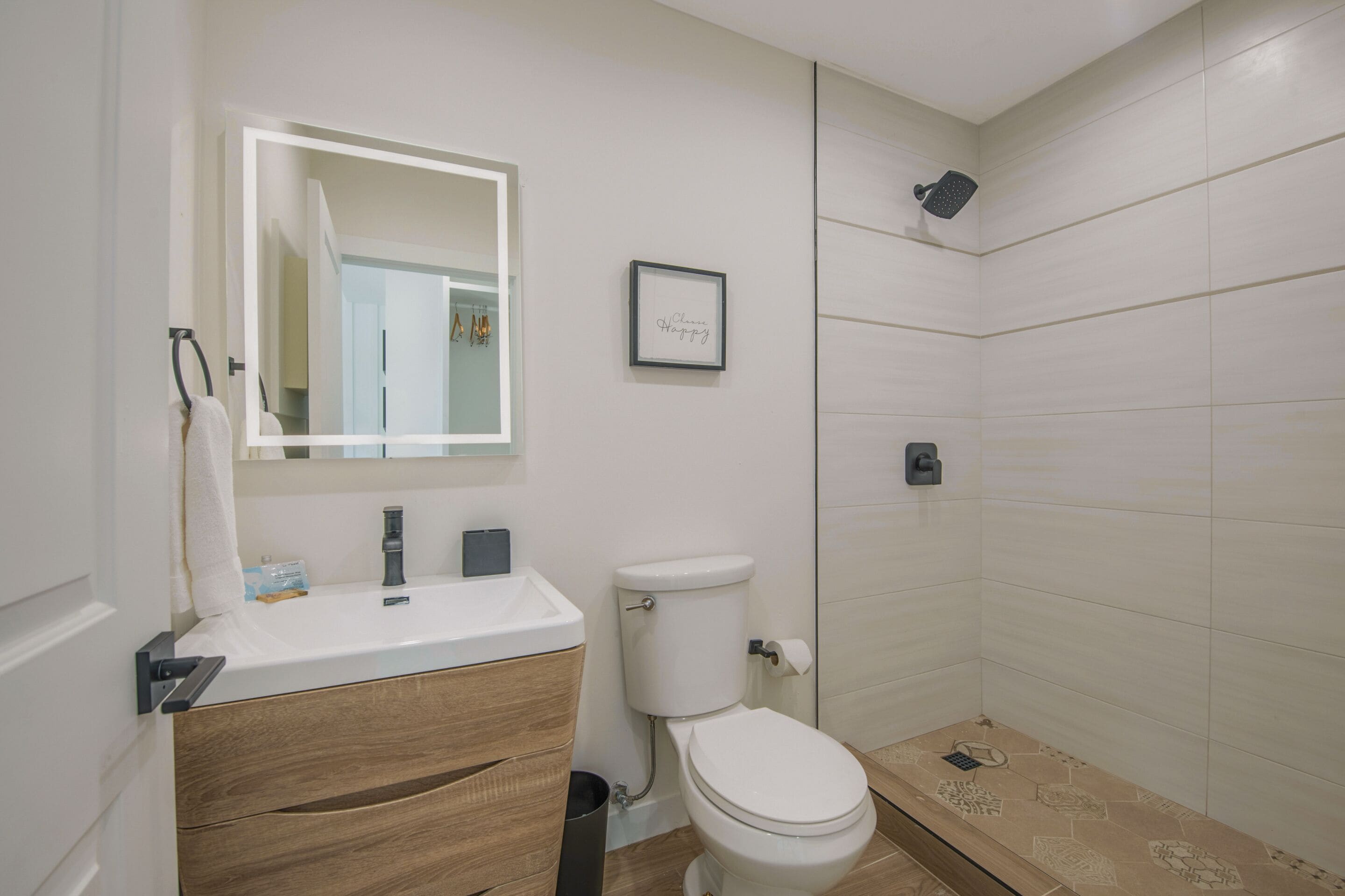 A modern bathroom with a white sink, wooden vanity, a toilet, and a shower area.