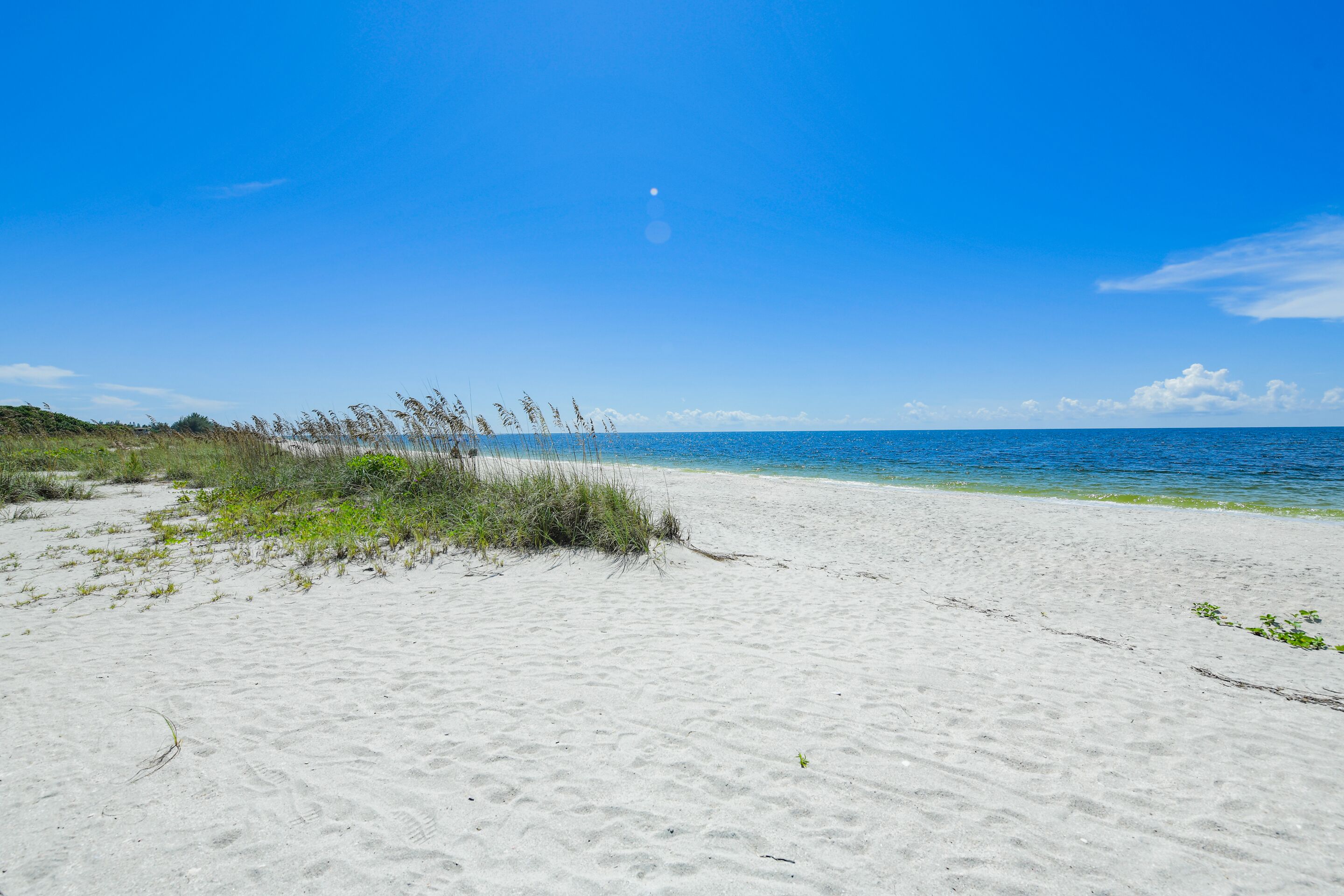 En sandstrand med kristallklart blått vatten och en klar himmel.