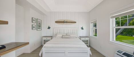 A bedroom with a bed, bedside tables, a ceiling fan, a window with a view, and a wall-mounted shelf.
