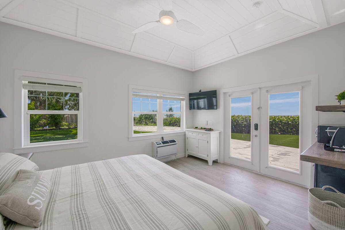A bedroom with a bed, a TV, a desk, and a view of a garden through the door.