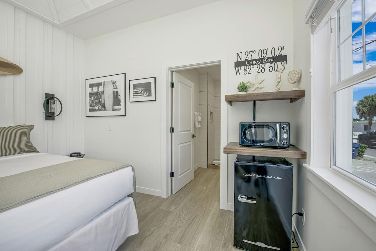 A compact hotel room with a bed, a small kitchenette with a microwave, and a door leading to another room.