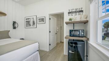 A compact hotel room with a bed, a small kitchenette with a microwave, and a door leading to another room.