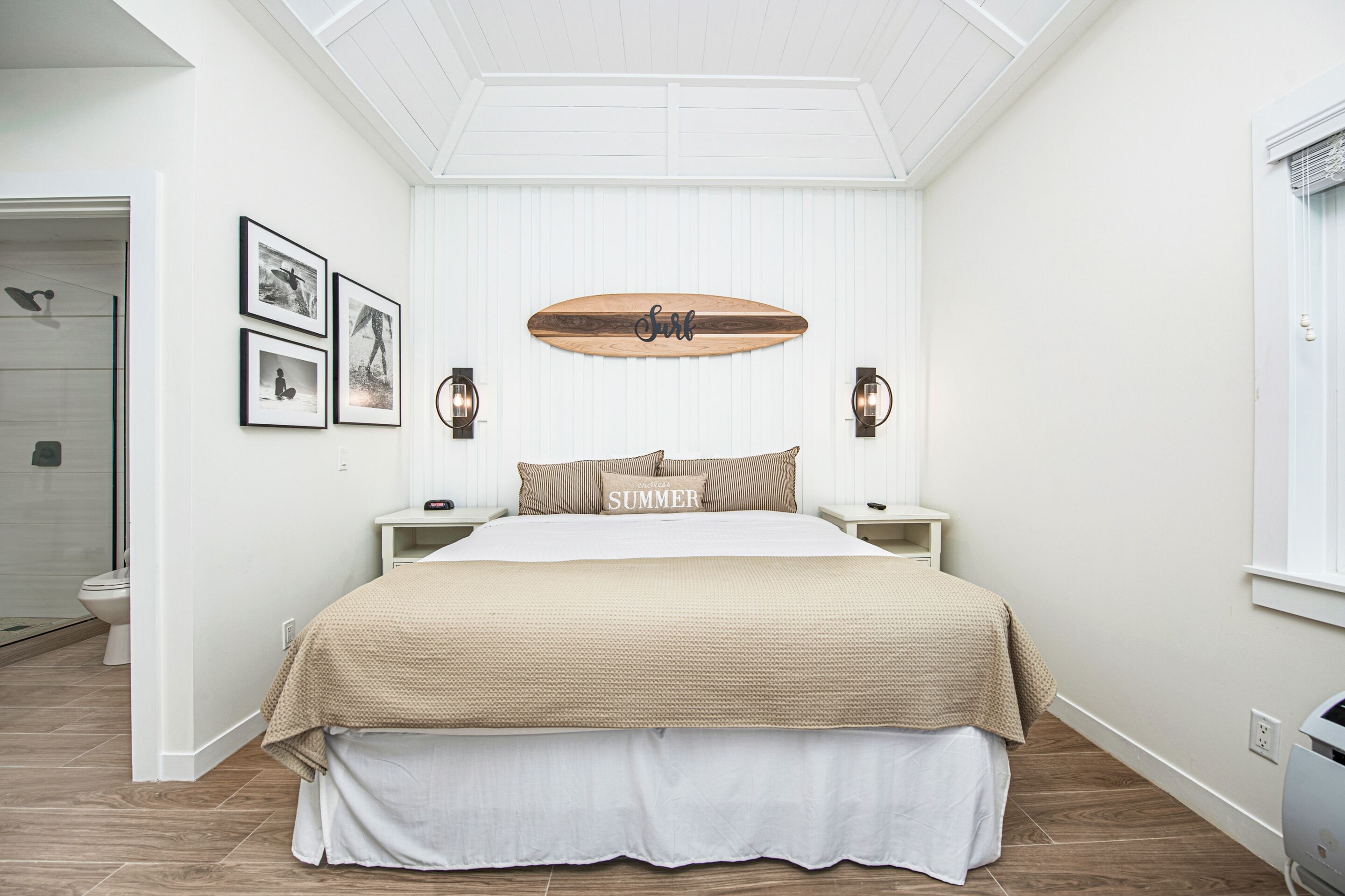 Une chambre avec un lit, une décoration murale représentant une planche de surf, des photos encadrées et une fenêtre.