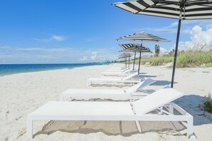 A beach with white lounge chairs and striped umbrellas.