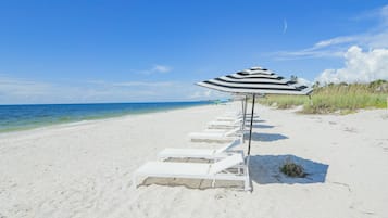 Una playa con sillas de descanso blancas y sombrillas a rayas alineadas a lo largo de la orilla.