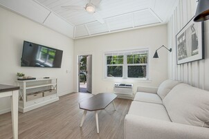 A living room with a flat-screen TV, a sofa, a coffee table, a TV stand, and a window with blinds.