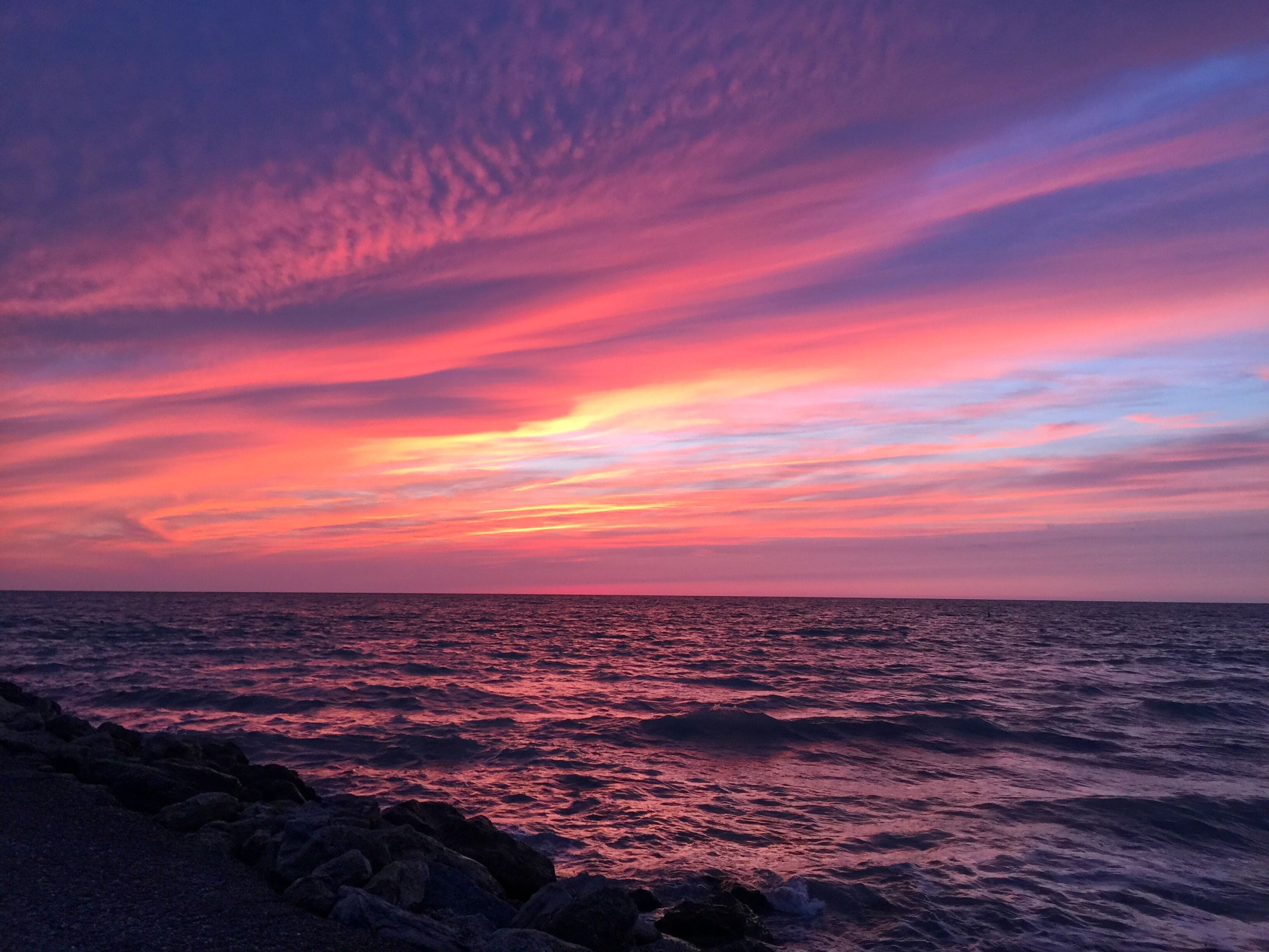 Un atardecer sobre el océano con una costa rocosa.