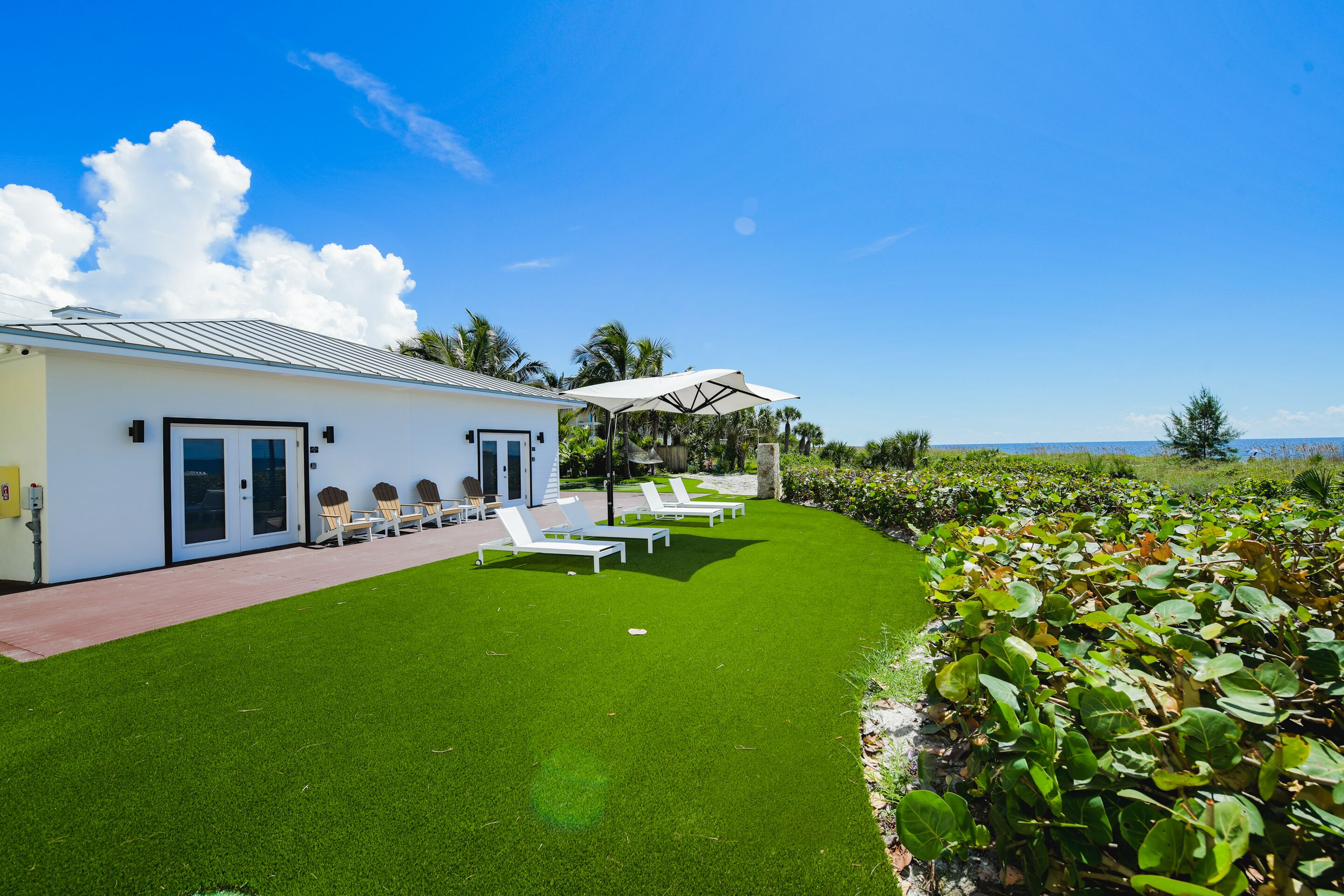 A modern building with a white exterior, a covered outdoor seating area with white lounge chairs, and a well-maintained lawn.