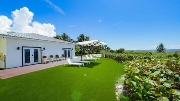 A modern building with a white exterior, a covered outdoor seating area with white lounge chairs, and a well-maintained lawn.