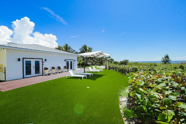 A modern building with a white exterior, a covered outdoor seating area with white lounge chairs, and a well-maintained lawn.