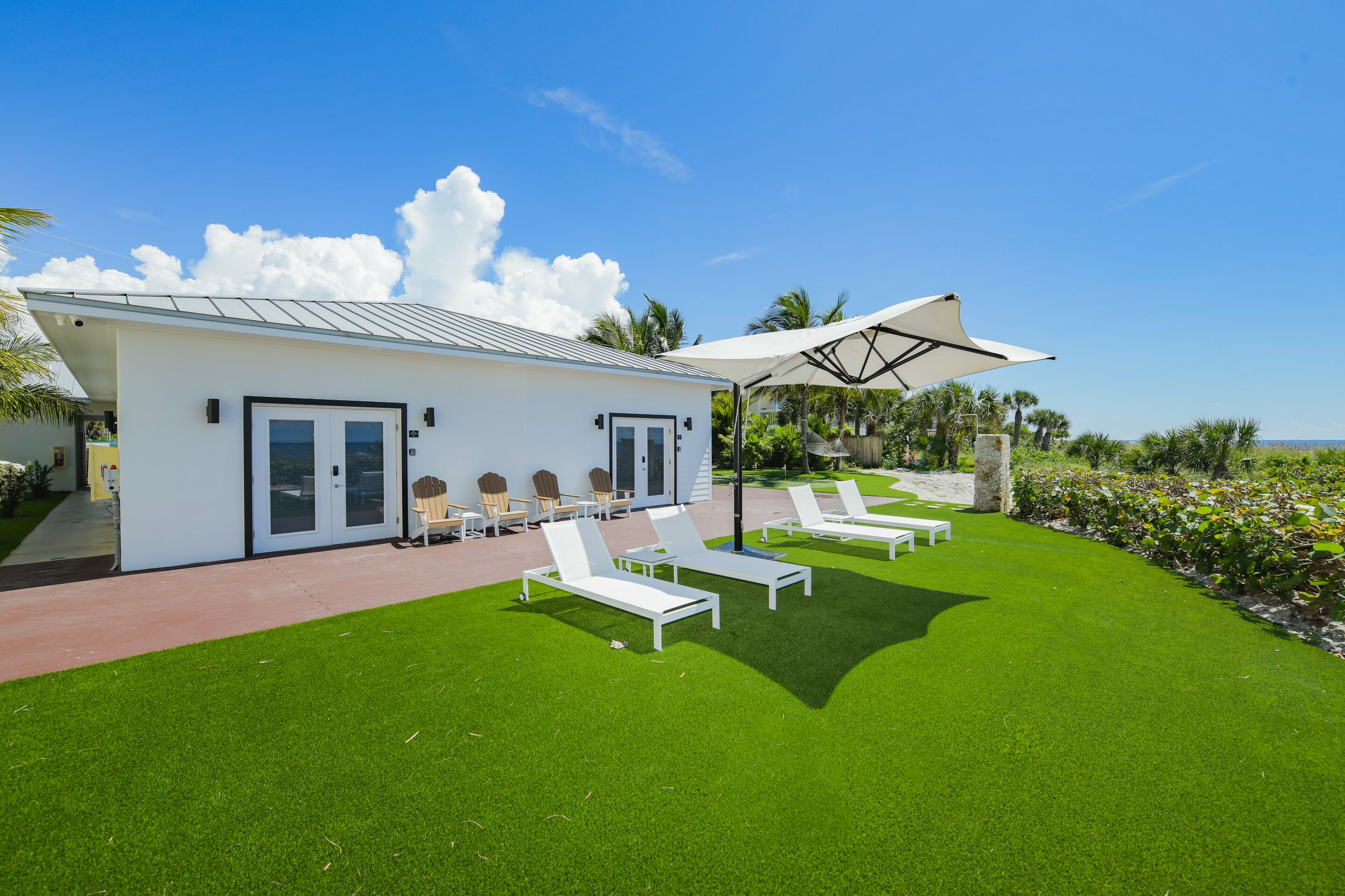 A modern house with a patio area featuring white lounge chairs and a large umbrella.