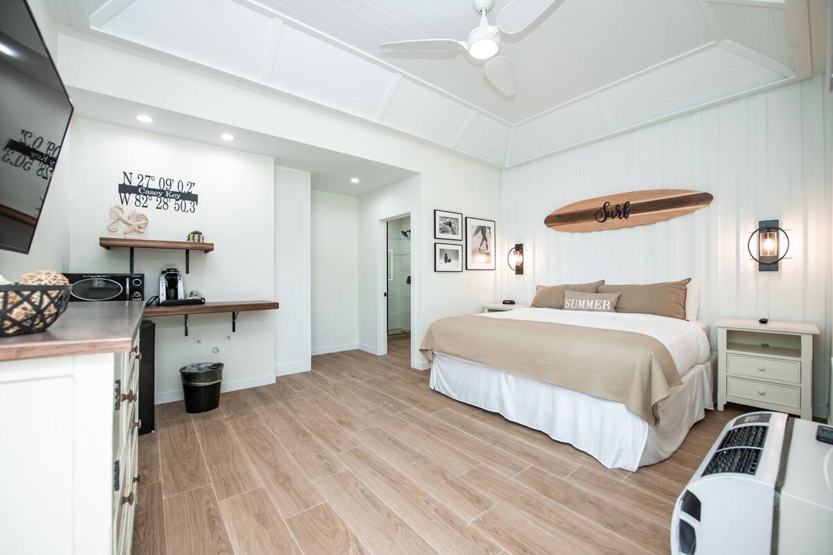 A bedroom with a bed, a ceiling fan, a surfboard decoration, and a wall with a map and pictures.