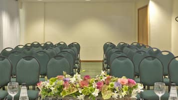 Un salón de conferencias con filas de sillas verdes, una mesa blanca con un centro de mesa floral y una puerta de madera al fondo.