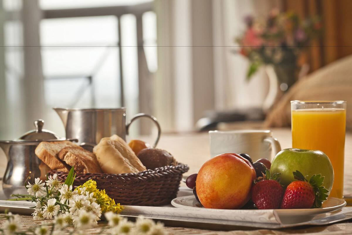 Ein Frühstücksbuffet mit Brot, Früchten und einem Glas Orangensaft auf einem Tablett.