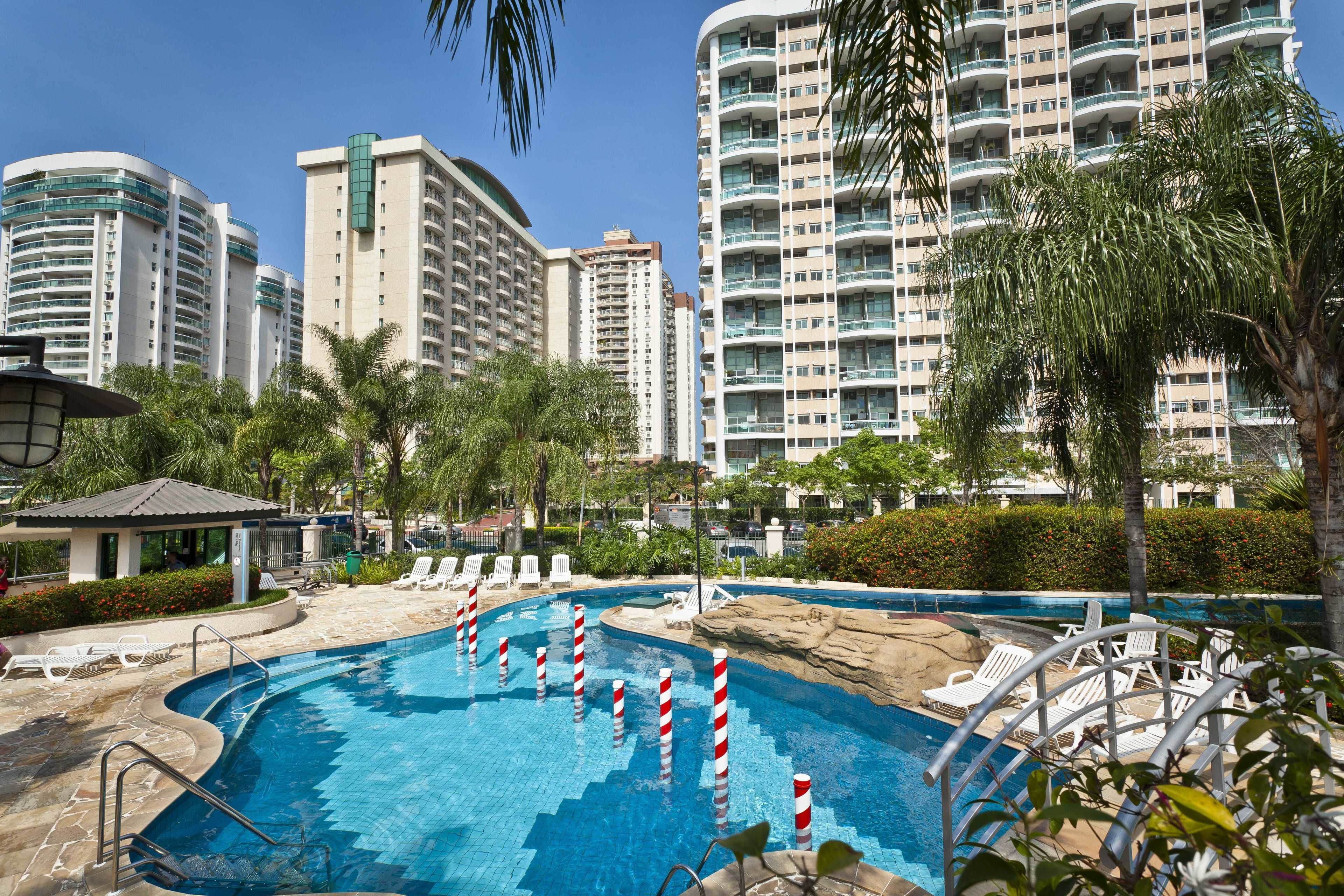 A swimming pool with lounge chairs and a gazebo, surrounded by palm trees and modern buildings.