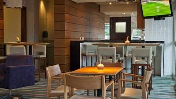 A modern dining area with a bar, wooden chairs, and a television mounted on the wall.