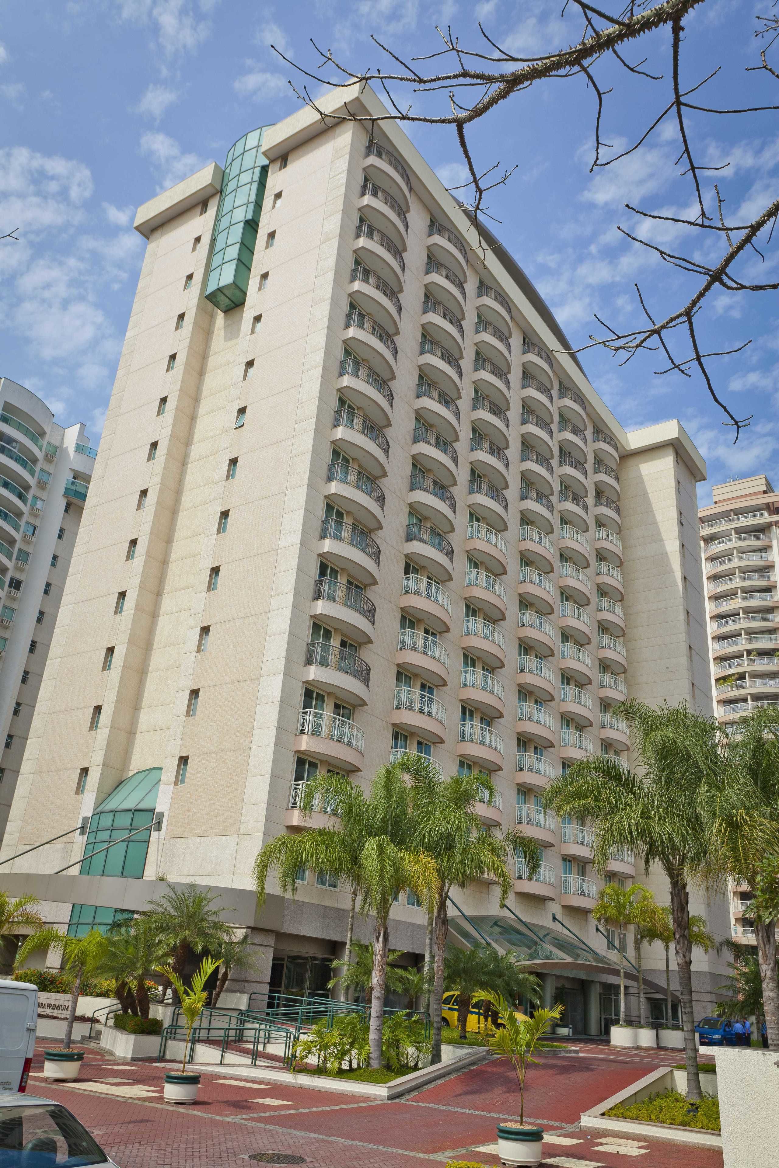 A high-rise hotel with multiple balconies, a curved facade, and a landscaped entrance area with palm trees.