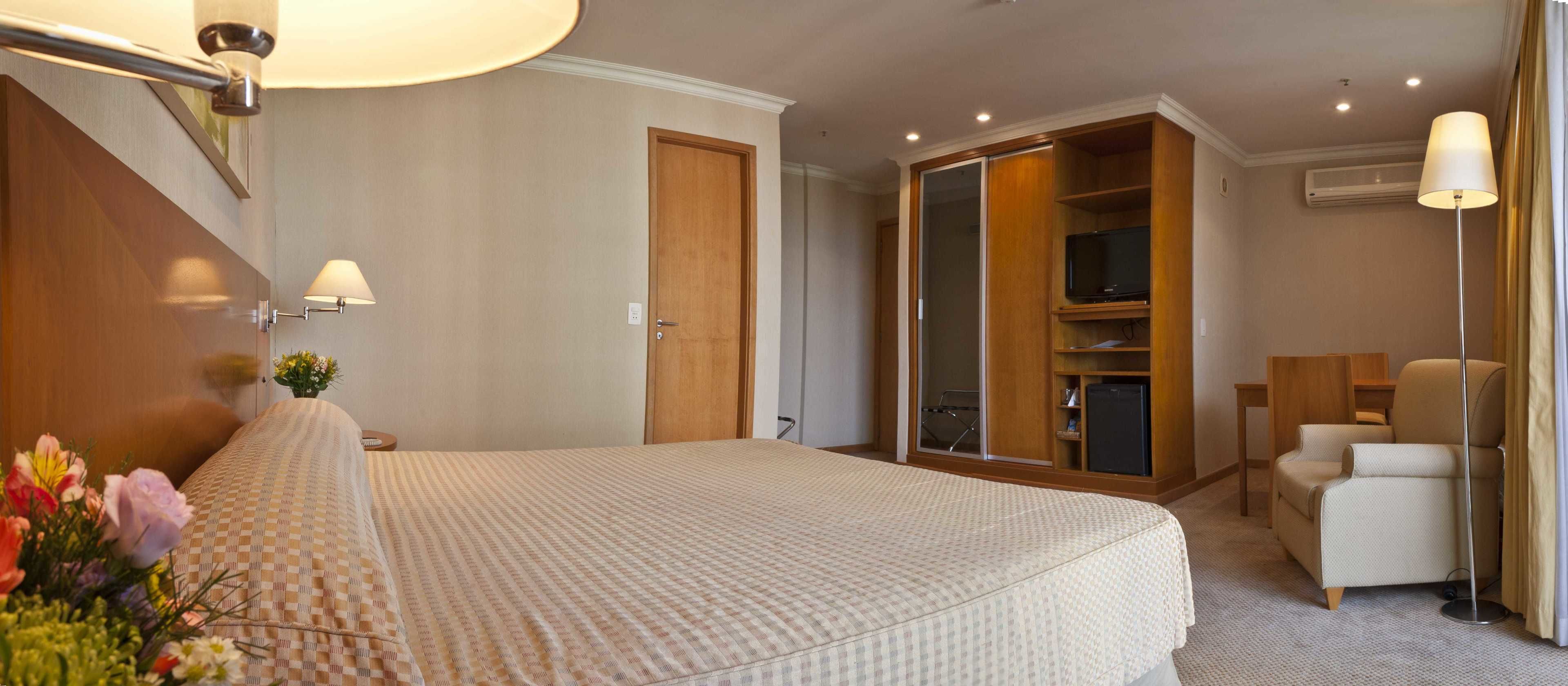 A hotel room with a large bed, a wardrobe, a television, and a seating area.