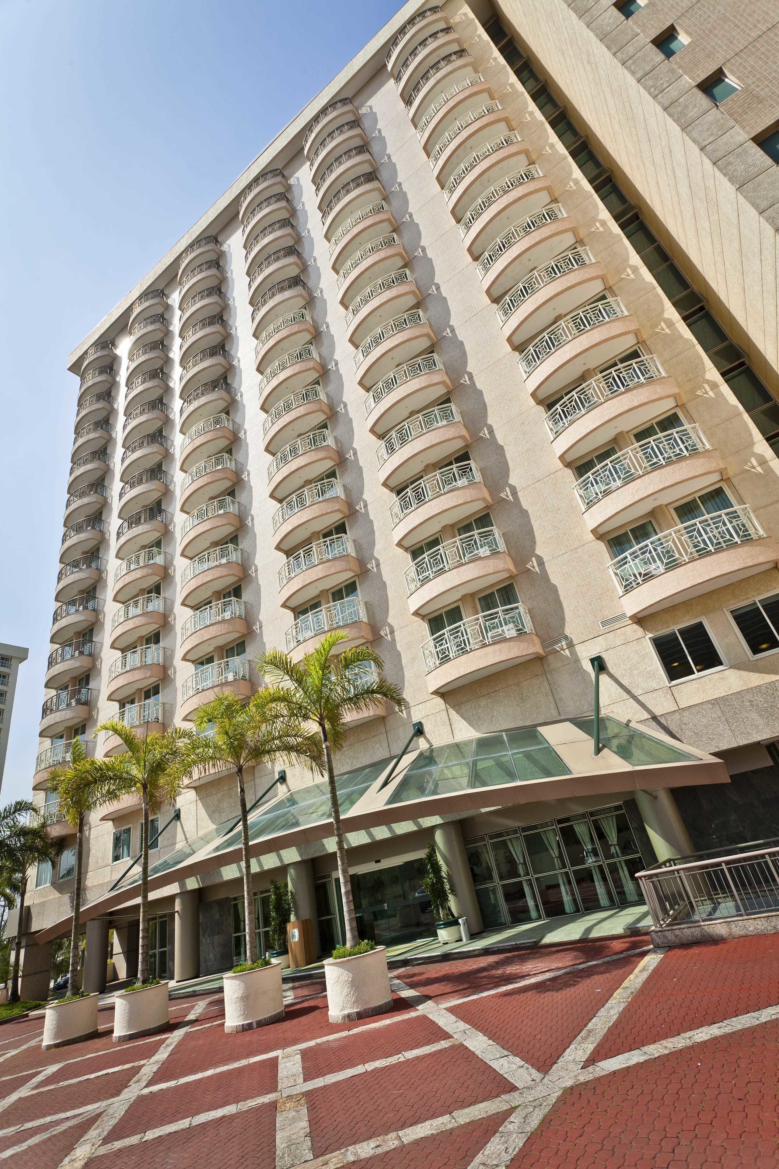 A high-rise hotel with multiple balconies, a modern entrance, and a red-bricked pavement.