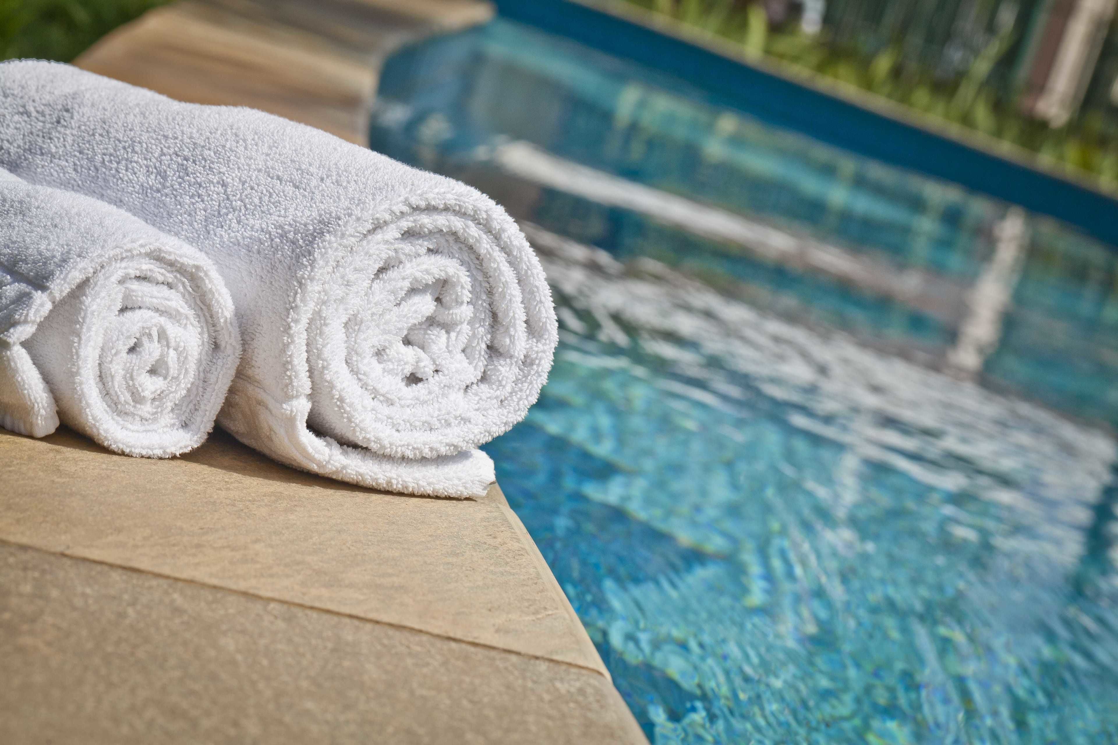 Two rolled white towels placed on a wooden ledge by a pool with clear blue water.