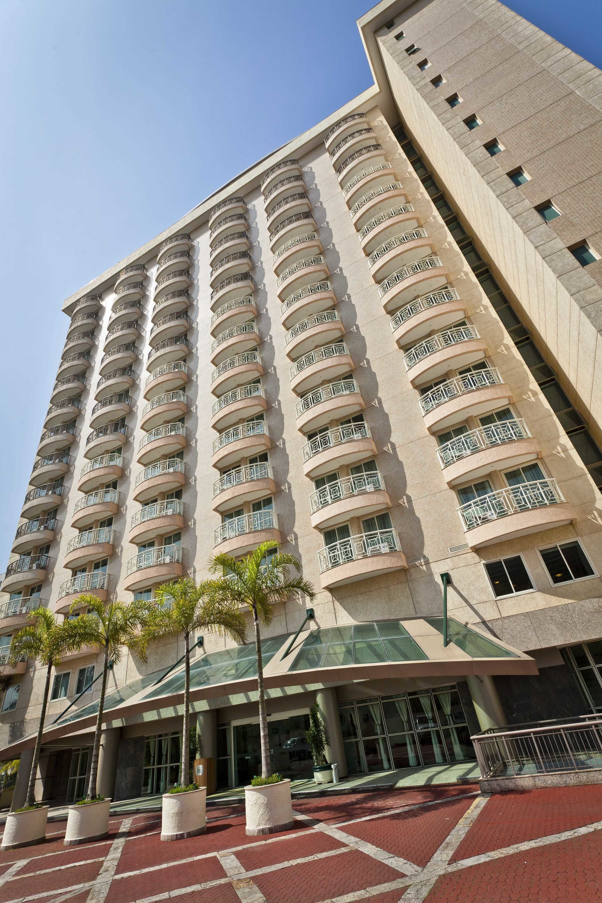A high-rise hotel with multiple balconies, a glass entrance, and a red brick ground floor.