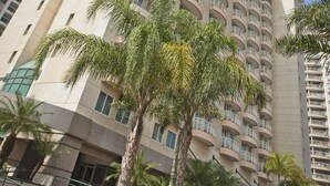 Un hotel alto de varios pisos con diseño moderno, con balcones en cada planta y rodeado de palmeras.
