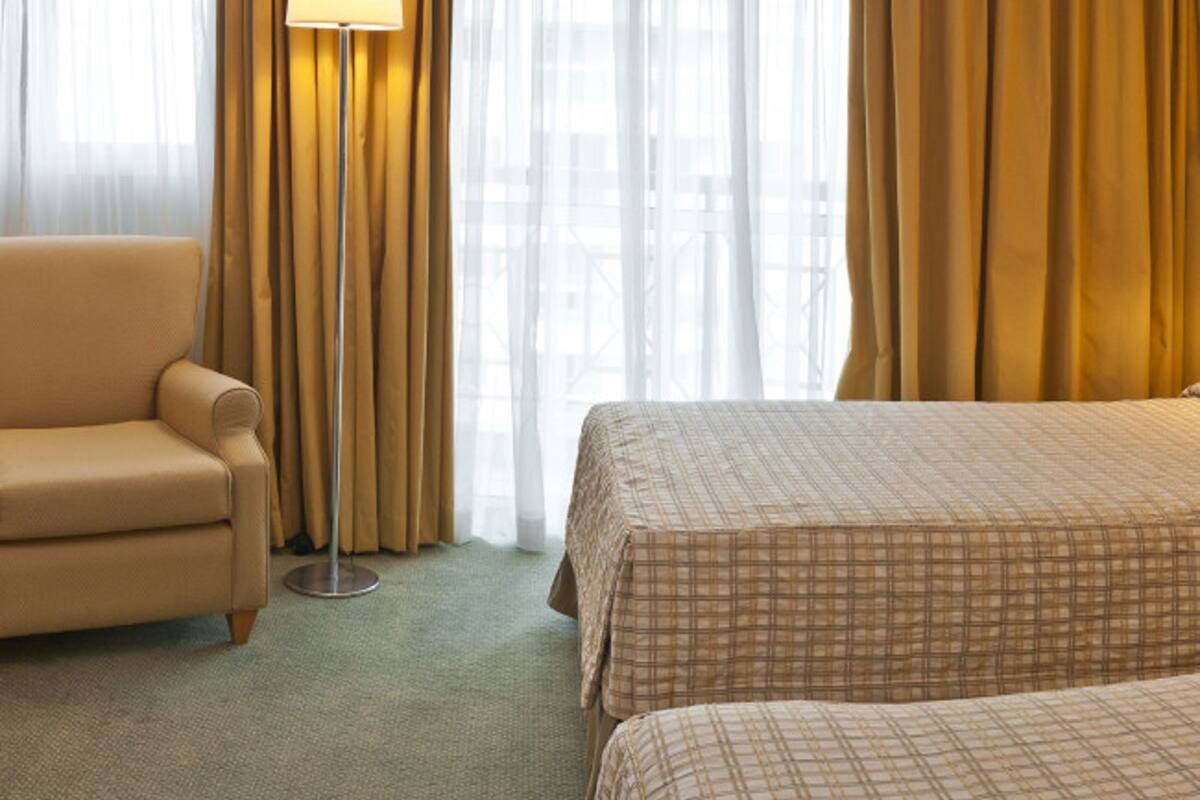 Ein Hotelzimmer mit einer Couch, zwei Betten, einer Lampe und transparenten Vorhängen.