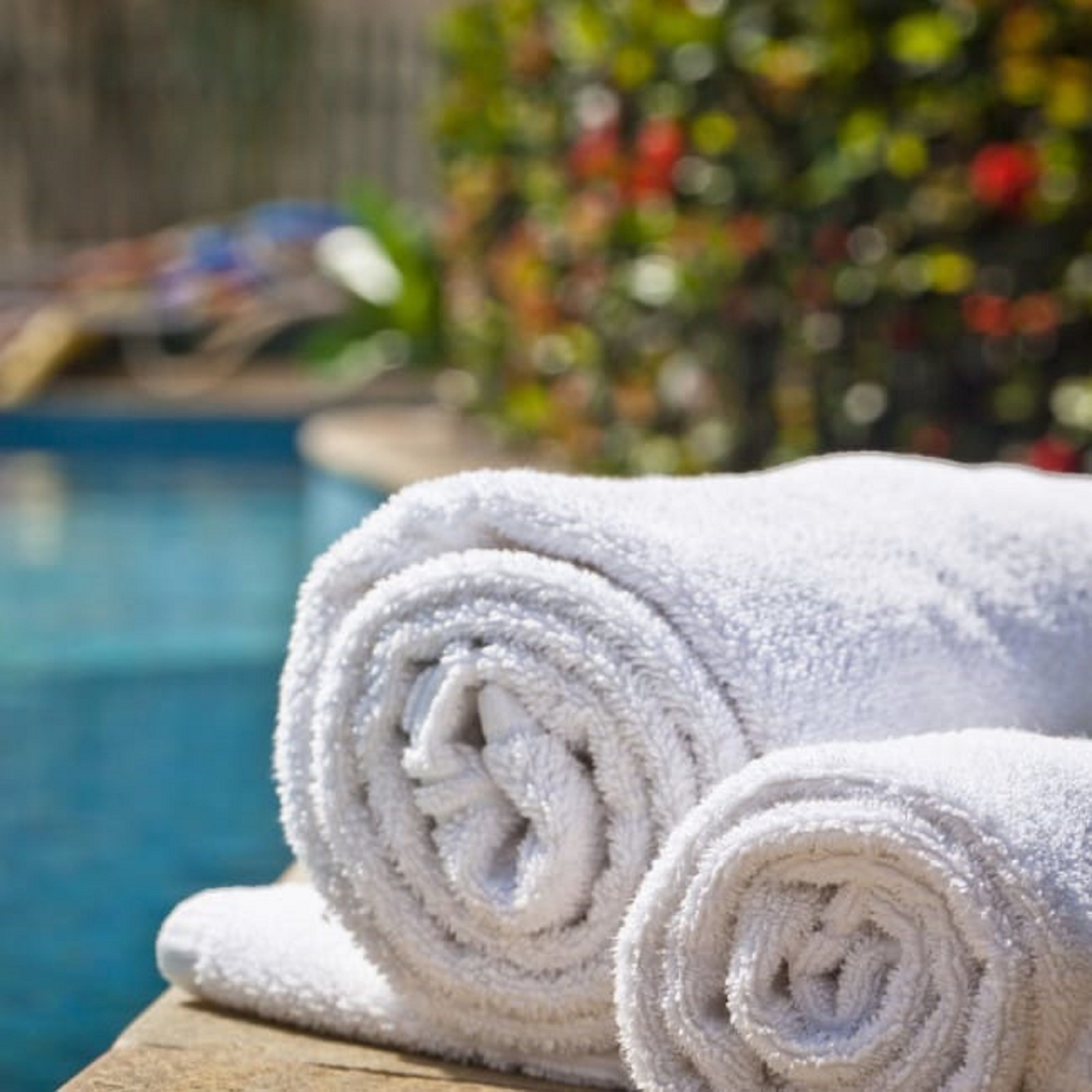 Two rolled white towels placed on a wooden surface near a swimming pool.