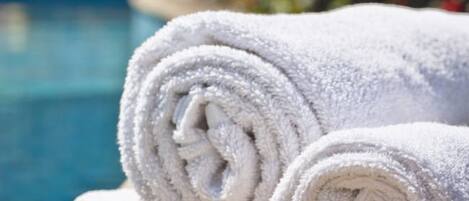 Two rolled white towels placed on a wooden surface near a swimming pool.