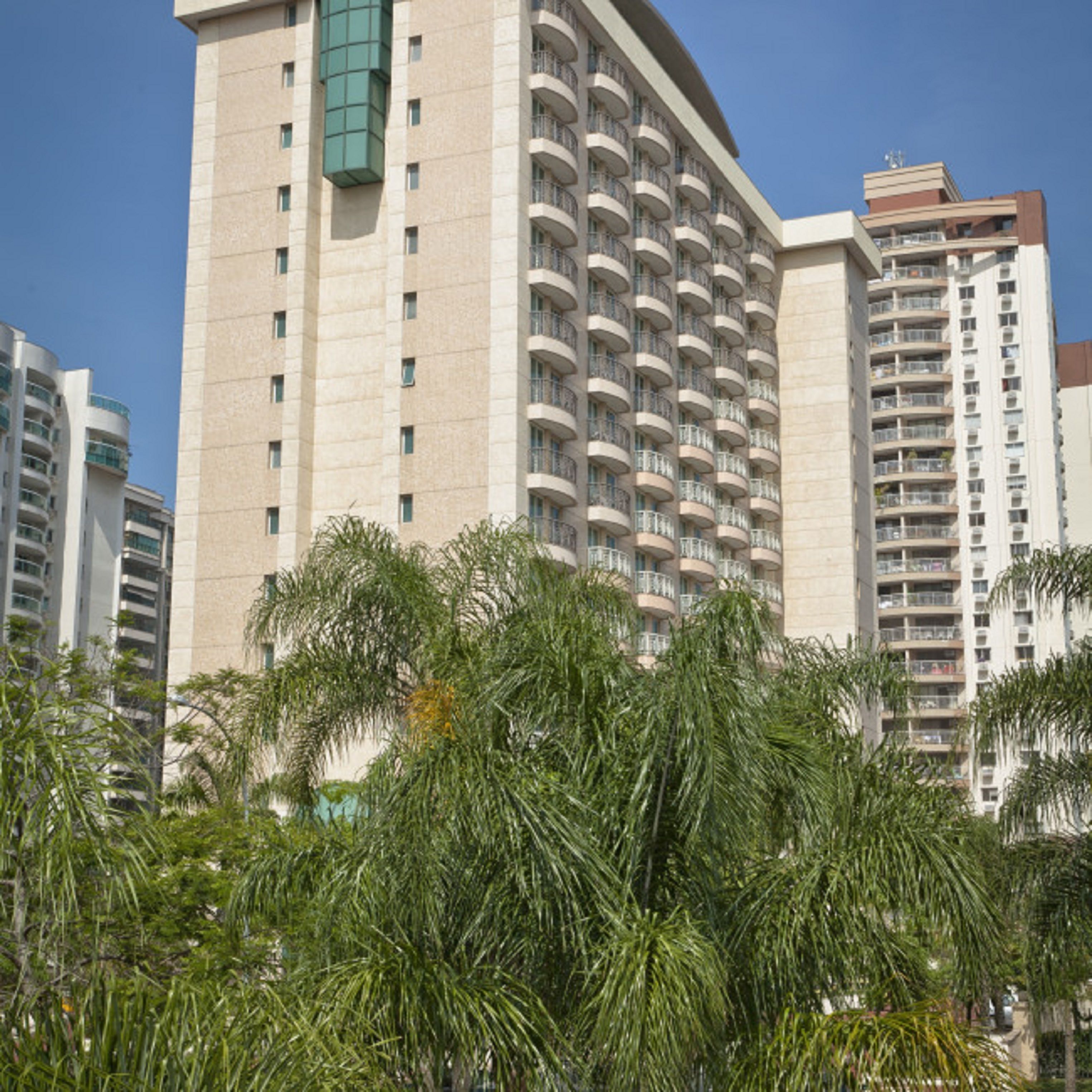 A high-rise hotel with multiple balconies, surrounded by palm trees.