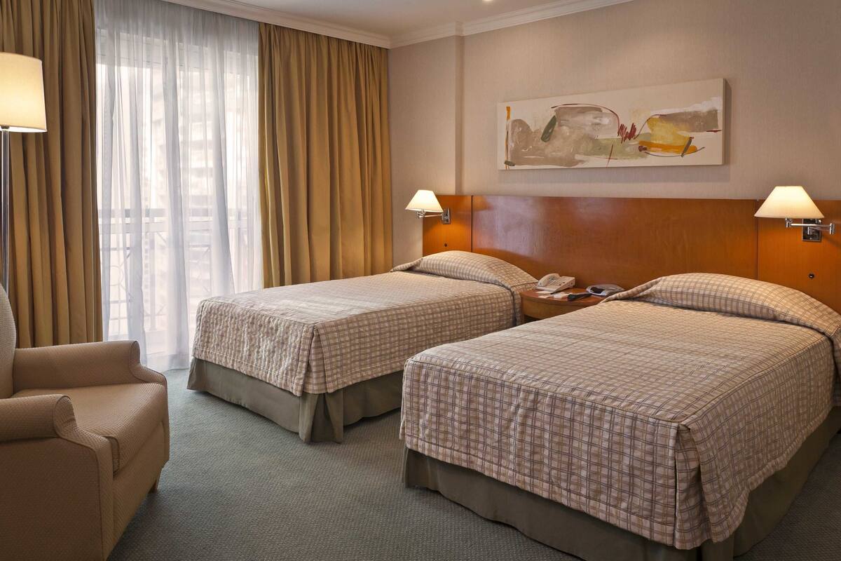Ein Hotelzimmer mit zwei Betten, einem Sessel, einer Lampe und einem Bild an der Wand.