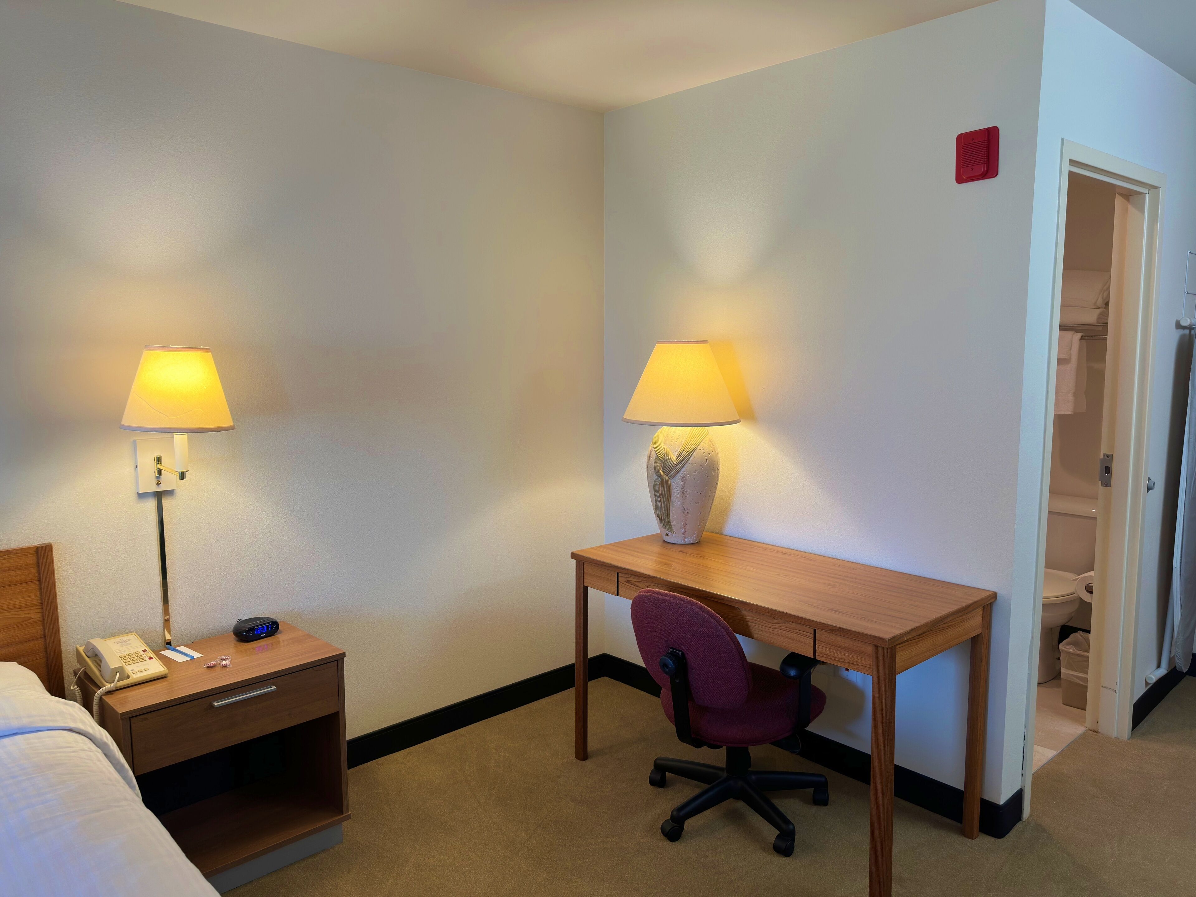 Hotelkamer met een bed, een bureau met stoel, een nachtkastje met telefoon en twee lampen.
