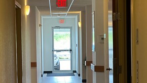 A long, narrow hotel corridor with a tiled floor, doors on both sides, and an exit sign overhead. - Peppermill Empress Inn (Centralia)