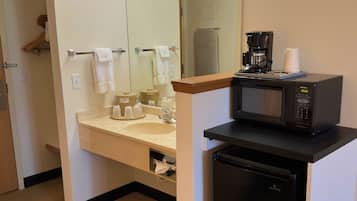 Une petite salle de bain d’hôtel comprenant un lavabo, un miroir et un petit réfrigérateur noir.