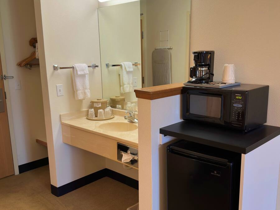 Une petite salle de bain d’hôtel comprenant un lavabo, un miroir et un petit réfrigérateur noir.
