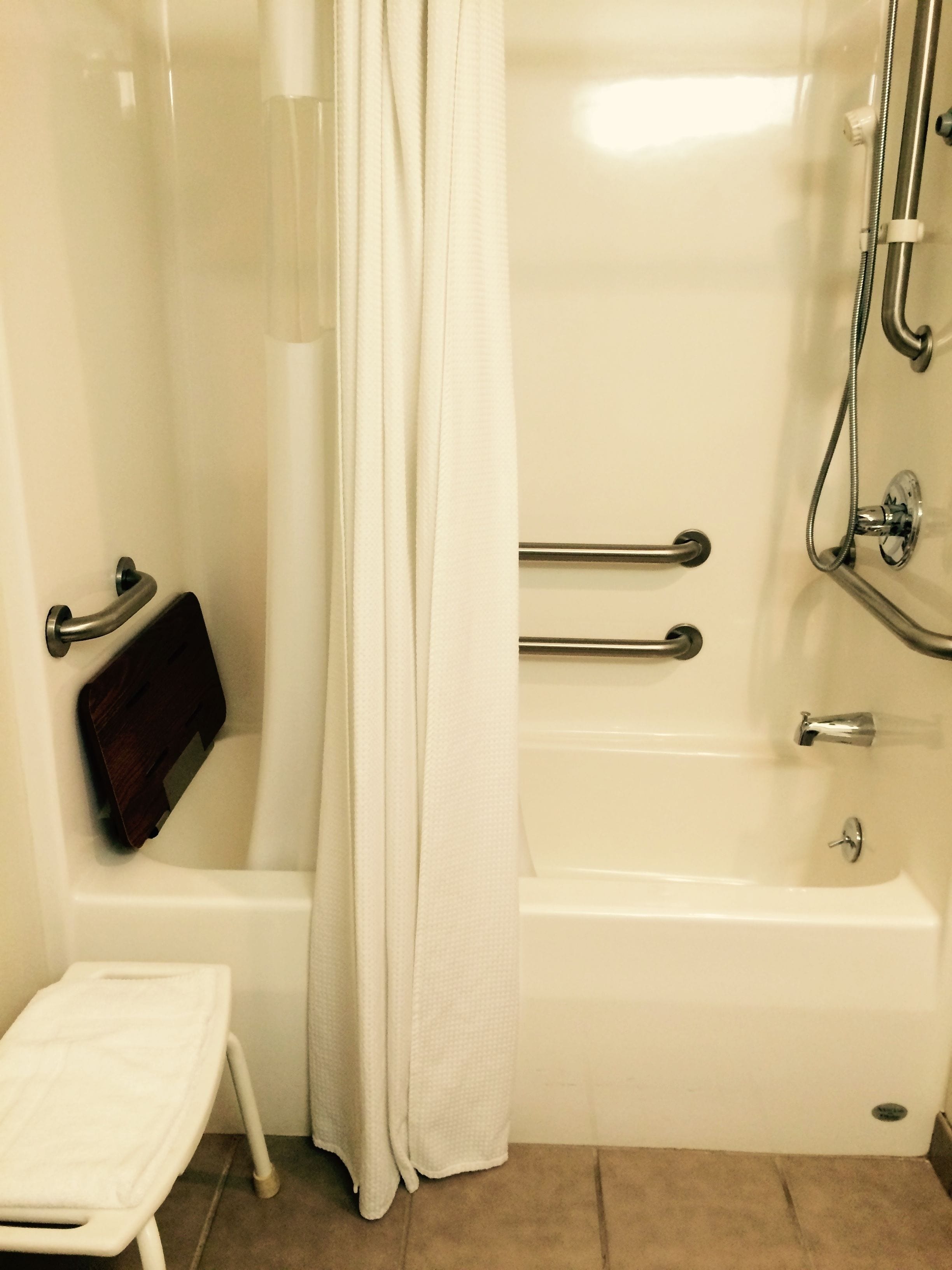 A bathroom with a bathtub, shower, and a small bench.