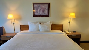 A neatly made bed with white linens, two bedside lamps, a framed artwork above the bed, and a wooden headboard. - Peppermill Empress Inn (Centralia)