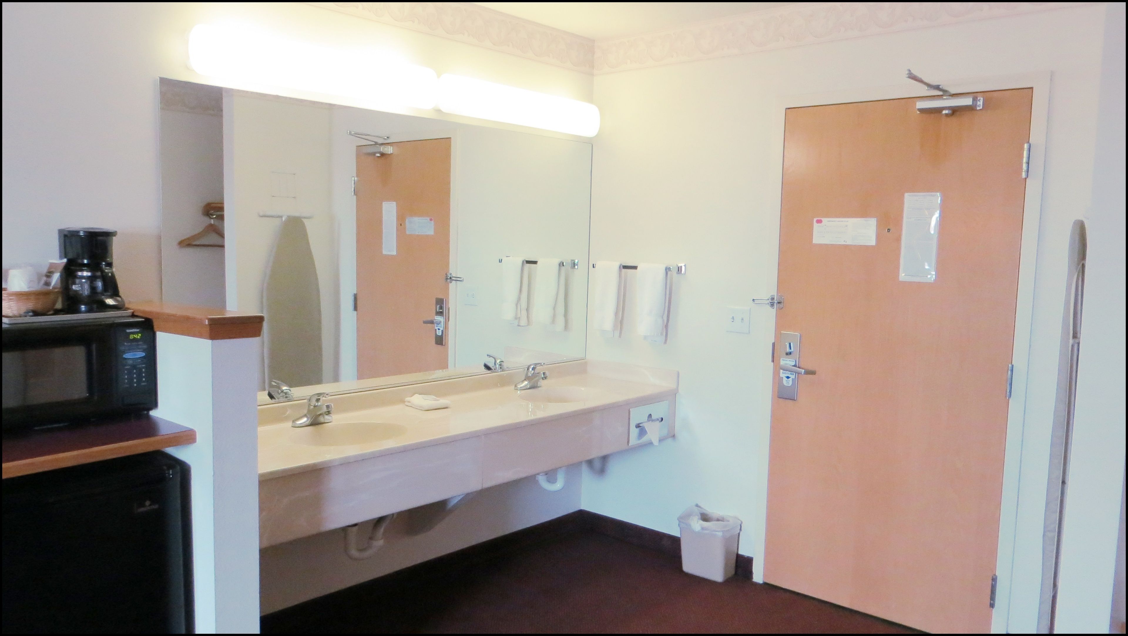A hotel bathroom with a sink, mirror, and a microwave on a shelf.